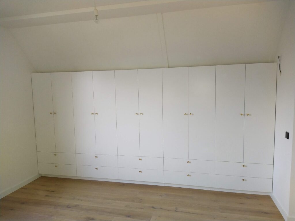 Kastenwand over de gehele breedte van een master bedroom, met geïntegreerde LED-verlichting en subtiele, ronde knoppen van massief geborsteld messing. Het middendeel van de kast, inclusief de laden, is uitneembaar en biedt toegang tot opbergruimte onder het dakschot! #kastopmaat #maatwerk #interieurbouw #abcoude #landvanwinkel #wardrobe #interior #interiordesign #masterbedroom #residential #residentialarchitecture #bespoke #bespokewardrobe #bespokefurniture #custommade @abcoude.nl